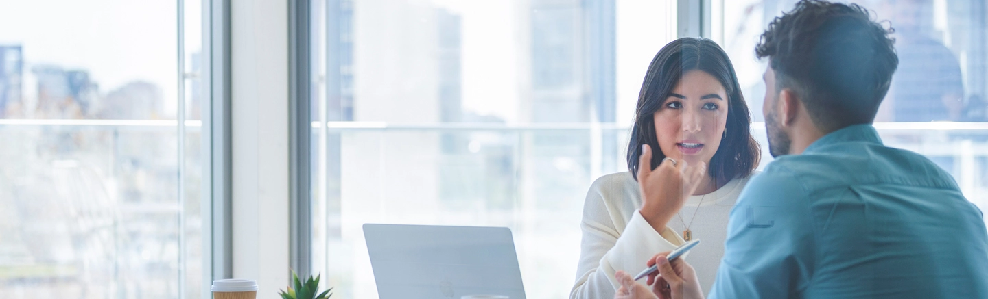 Woman in white shirt talking to man at table with laptop