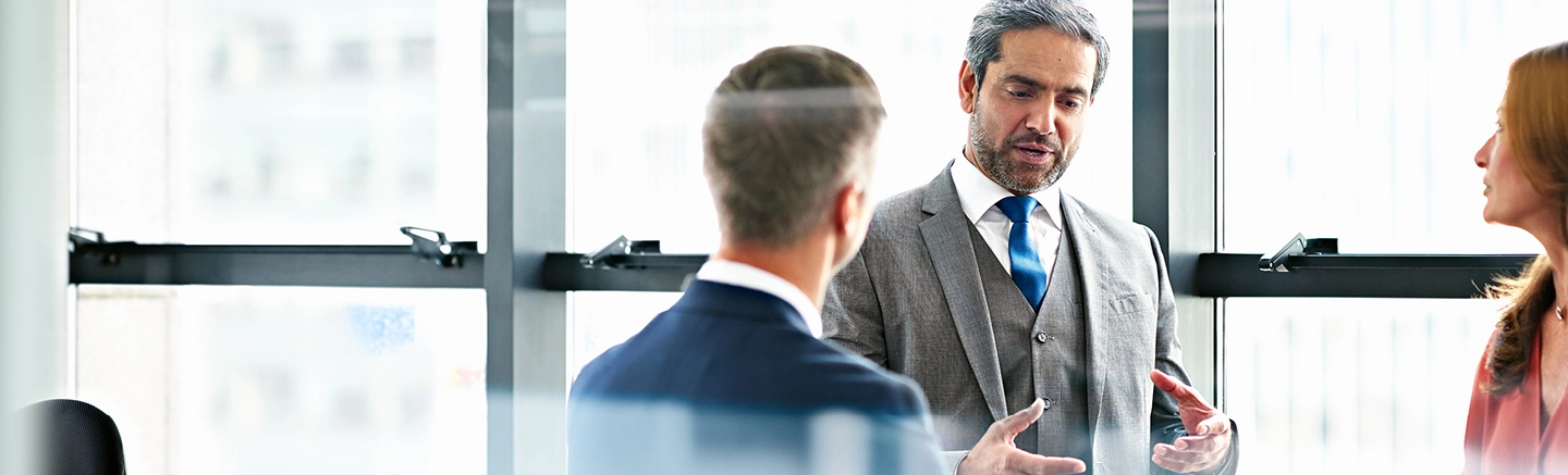 Colleagues in a meeting room with older man in grey full piece suit talking