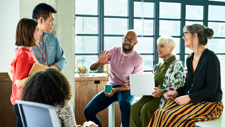 A group of people listen to a man in a meeting inside an office.