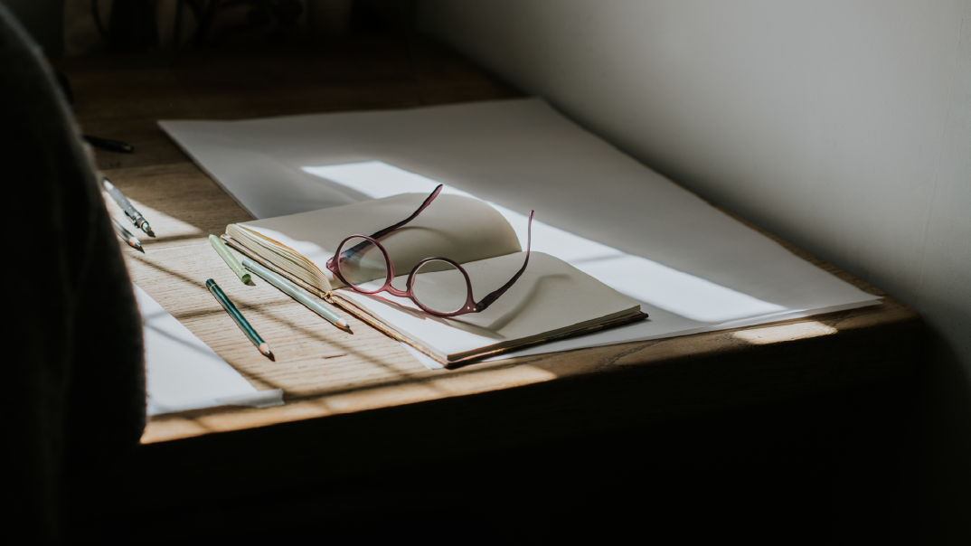 A picture of an open blank book with pink glasses on top and different colored pencils.