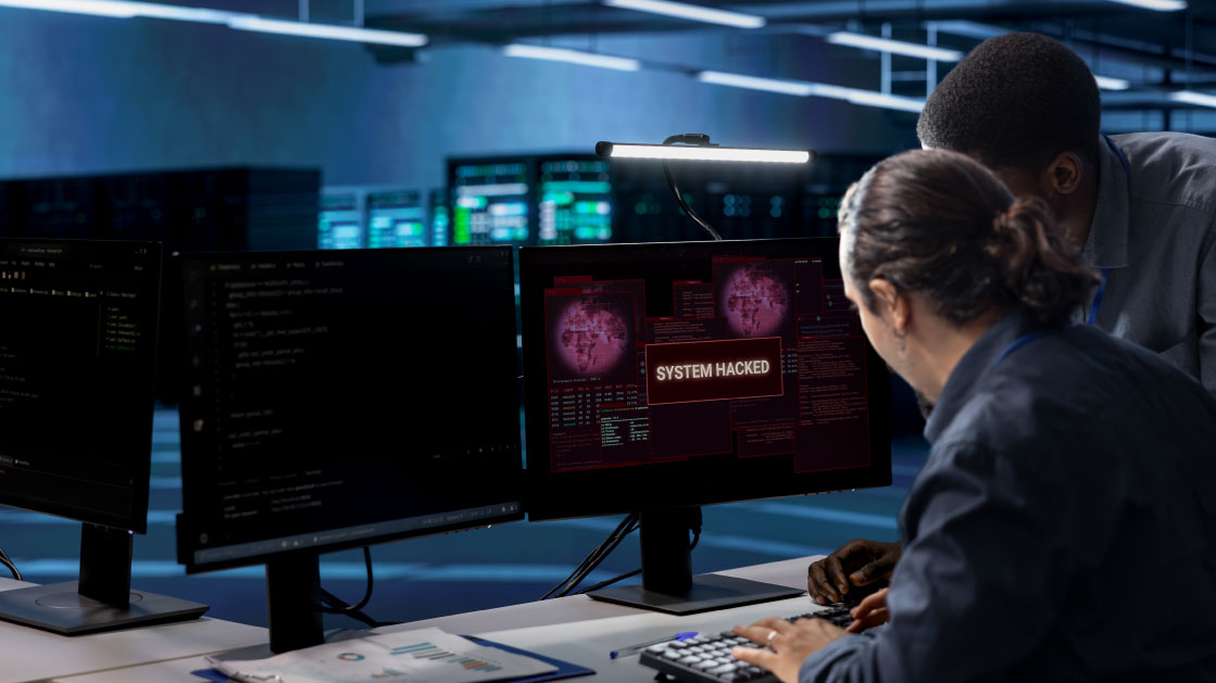 Two men in an obscure data center look into two monitors, one which is displaying a red screen with the words: 