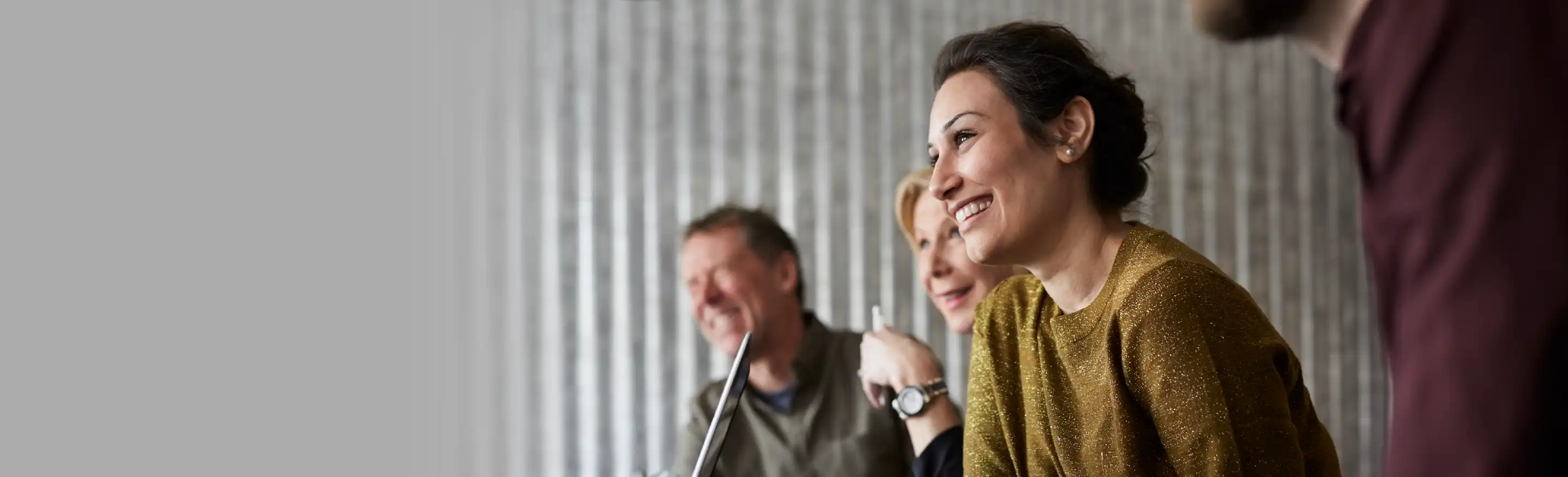 Business team meeting around a table with corrugated metal wall background, collaborative discussion in modern office setting.