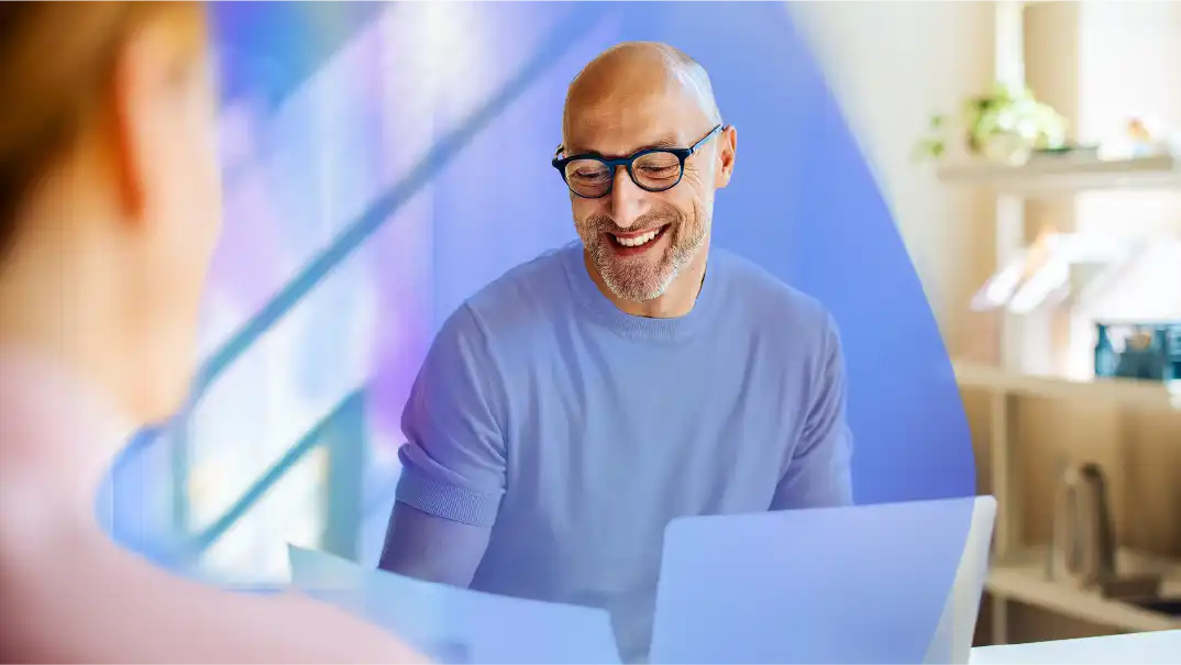 Ace your interview with our guide for job seekers: A man smiles as he looks at his resume with his laptop next to him. He is working from home.