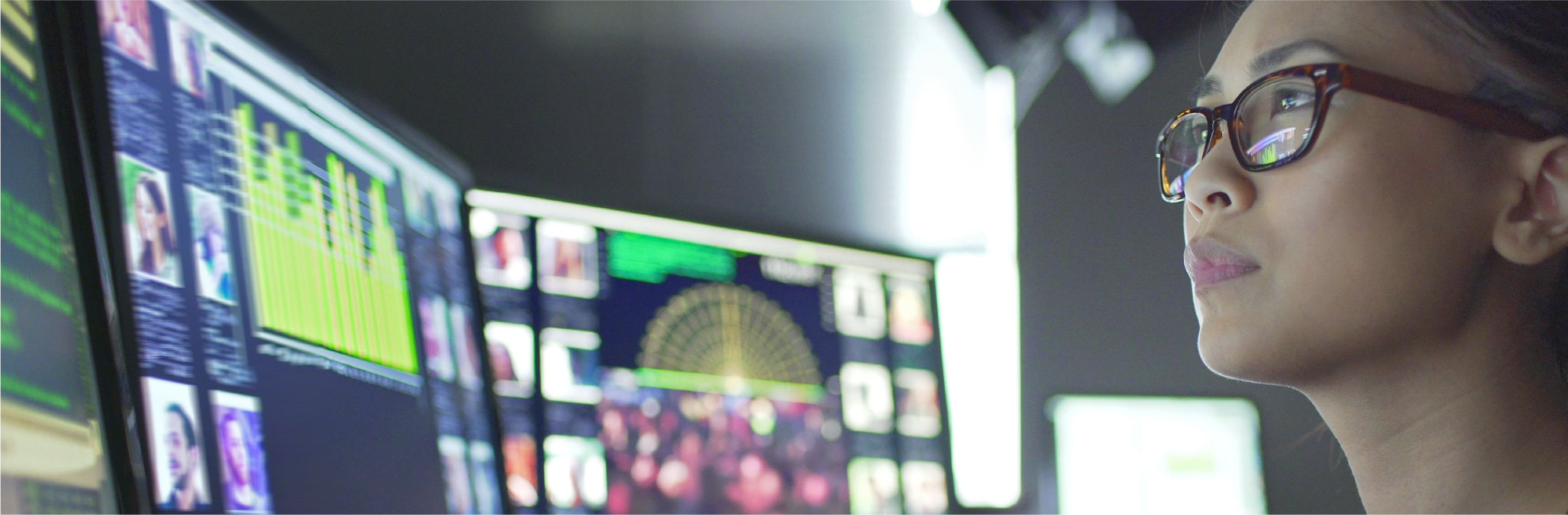 Multiple computer monitors displaying data visualizations, graphs, and images in a dimly lit workspace.