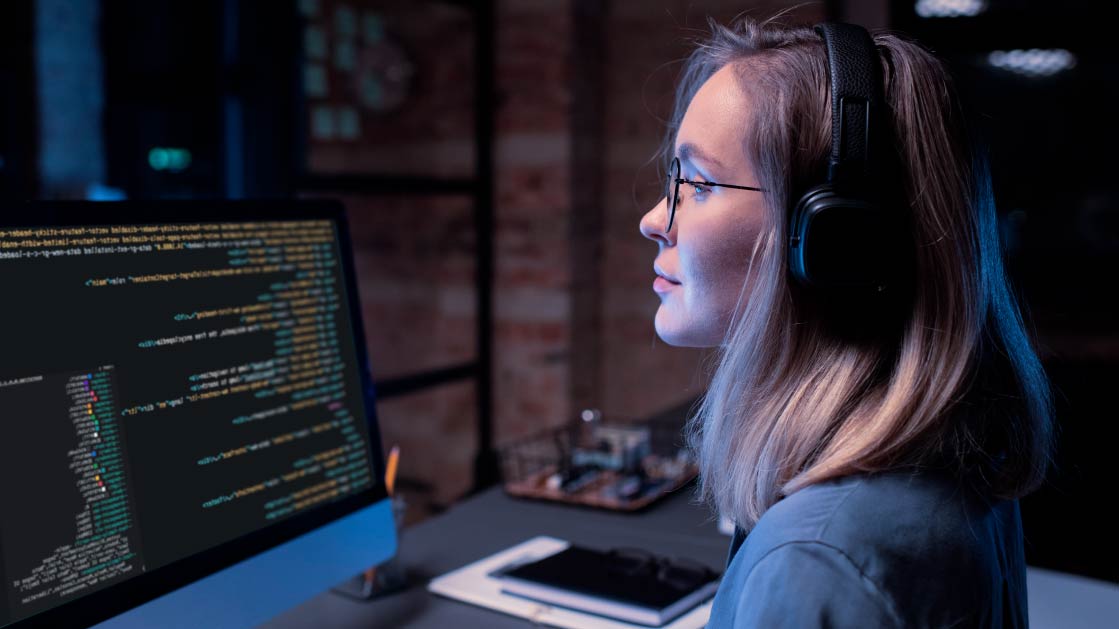 Woman wearing a headset and working on computer which is displaying coding on the screen