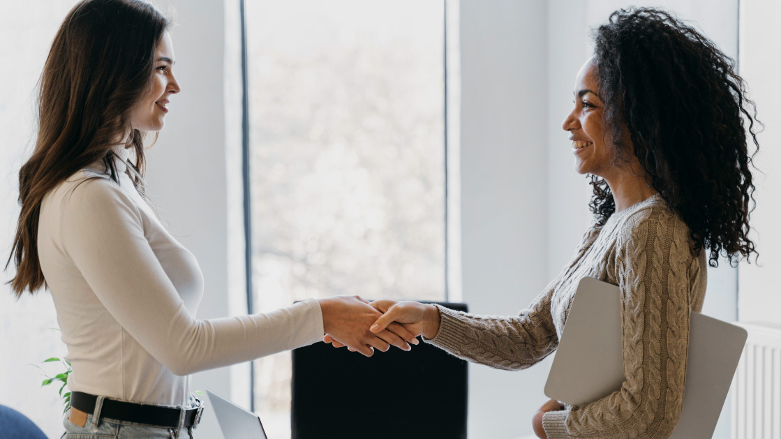 Two women shake hands as they smile at each other.