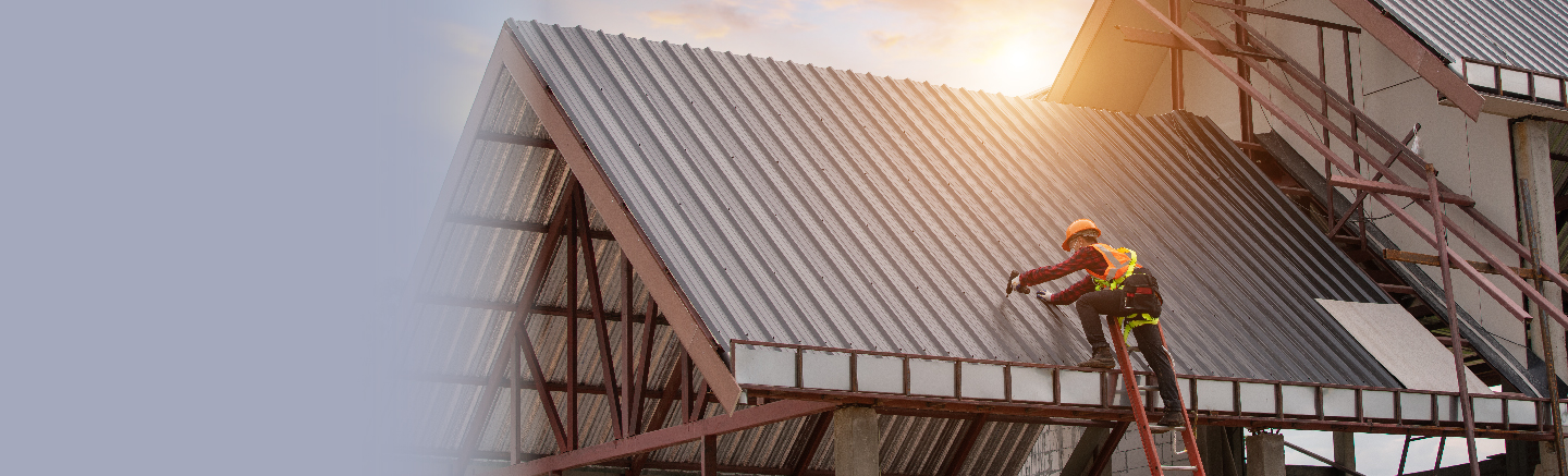  Worker with a drill on a roof in construction clothing and gear including a bright orange hard hat and security vest.