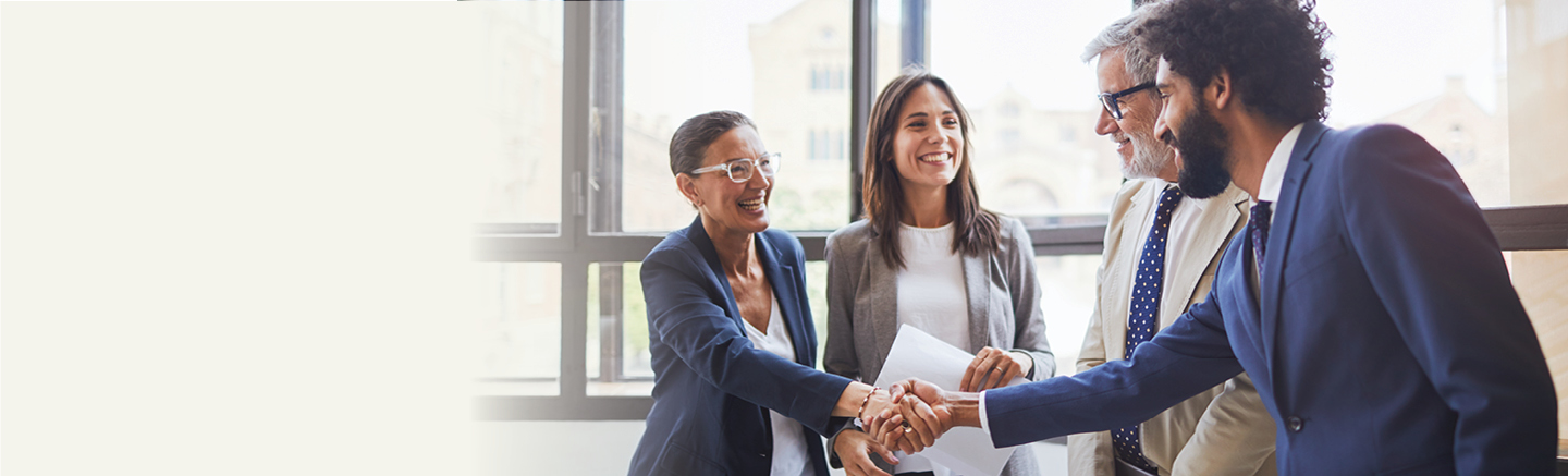 In a group of four people inside and office, two of them shake hands with a smile.