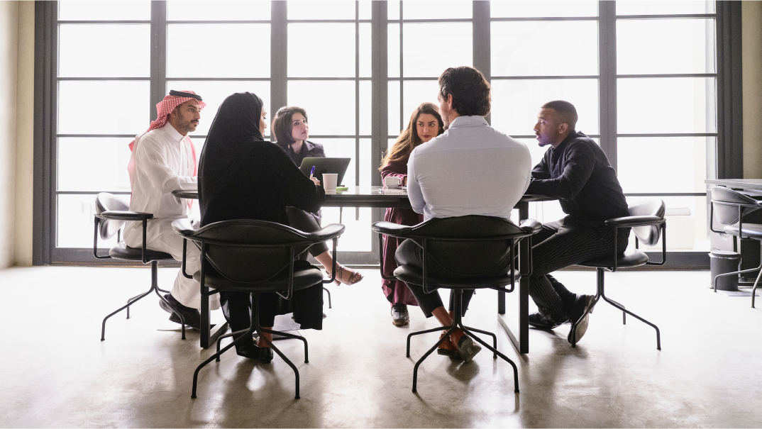 A group of people sit in an office for a meeting.