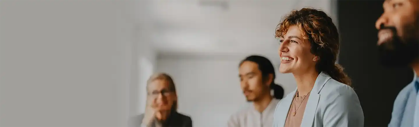 A group of people sitting and standing in a room, engaged in a discussion or meeting. The background is blurred, drawing attention to the individuals in the foreground.