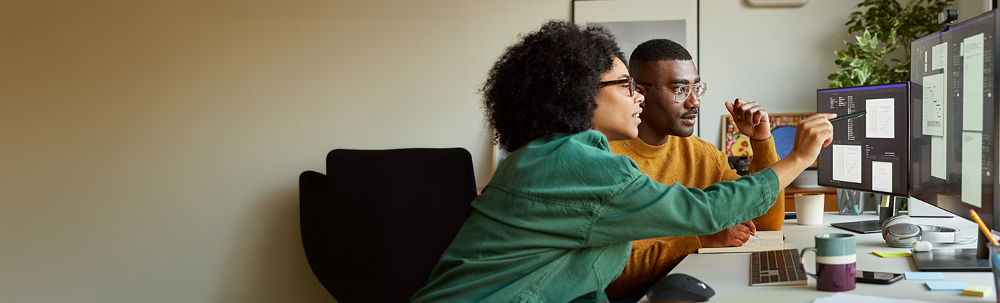 Woman pointing at double monitor with black man beside her